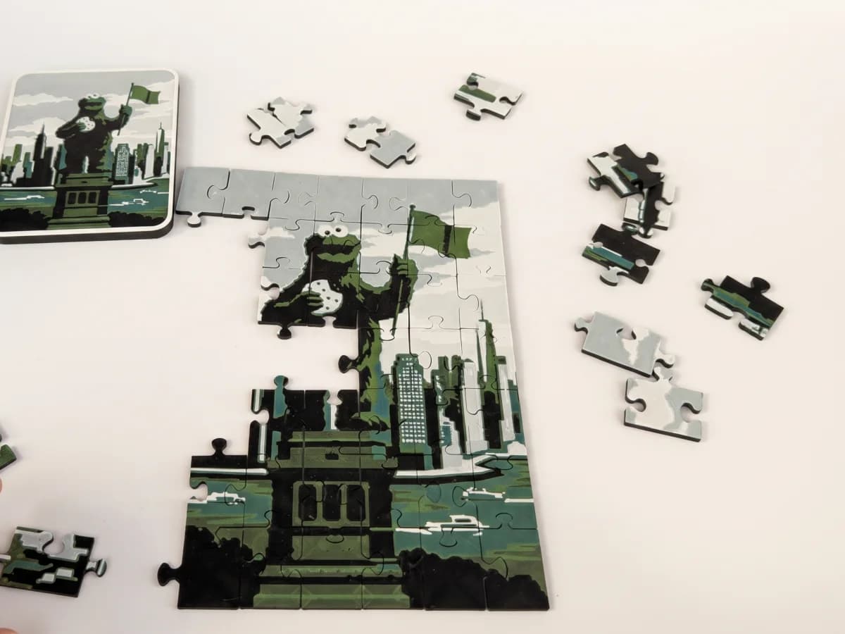 A photo puzzle half assembled next to its gift box lid, with loose pieces waiting around it