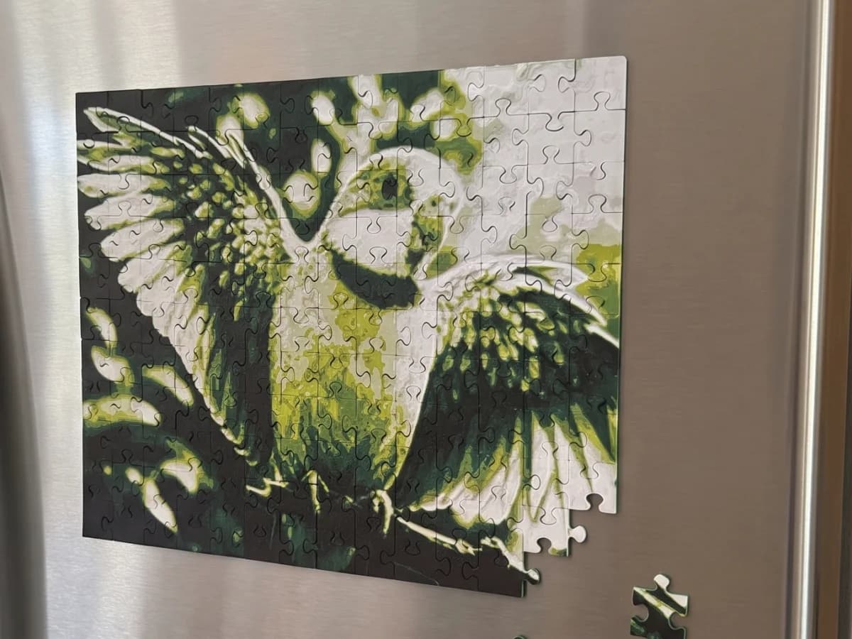 3D printed photo puzzle held on a stainless steel fridge by magnets, a few loose pieces stuck beside it